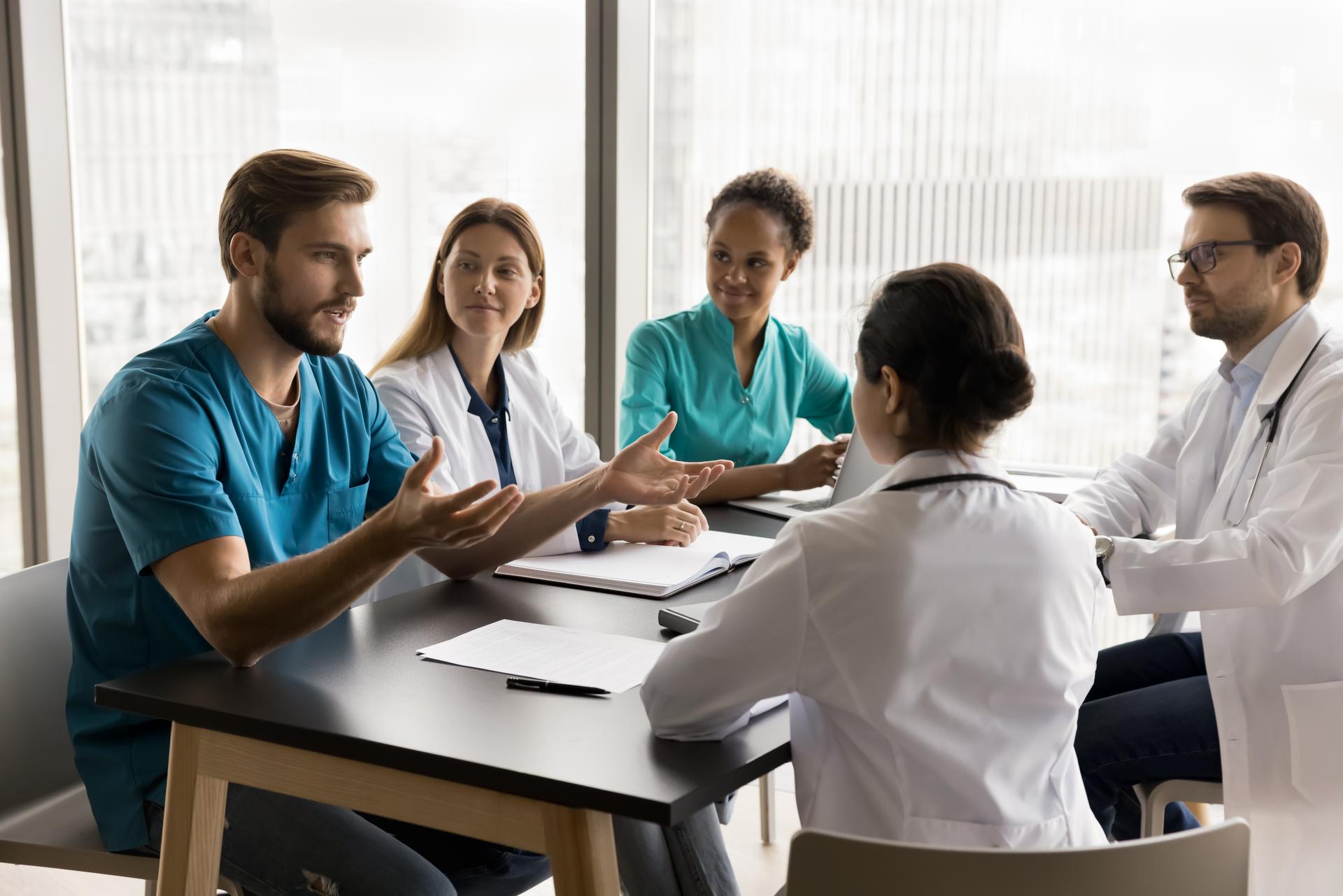 Confident young surgeon man in uniform talking to multiethnic colleagues