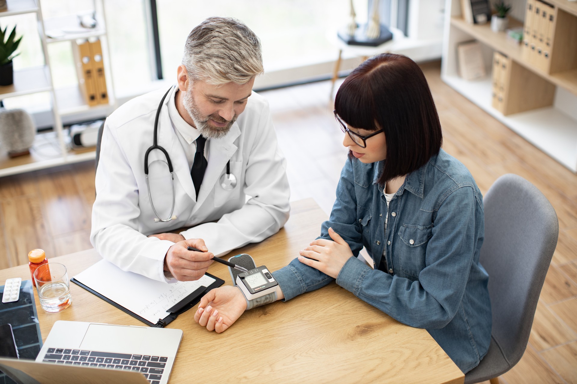 Physician and woman monitoring tonometer on wrist in office